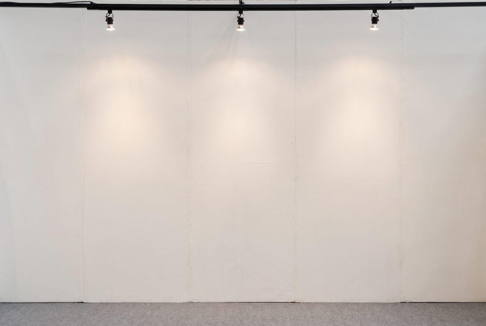 Visuel d'ambiance : un long mur blanc éclairé par une rampe de projecteurs, dans une salle vide au sol clair