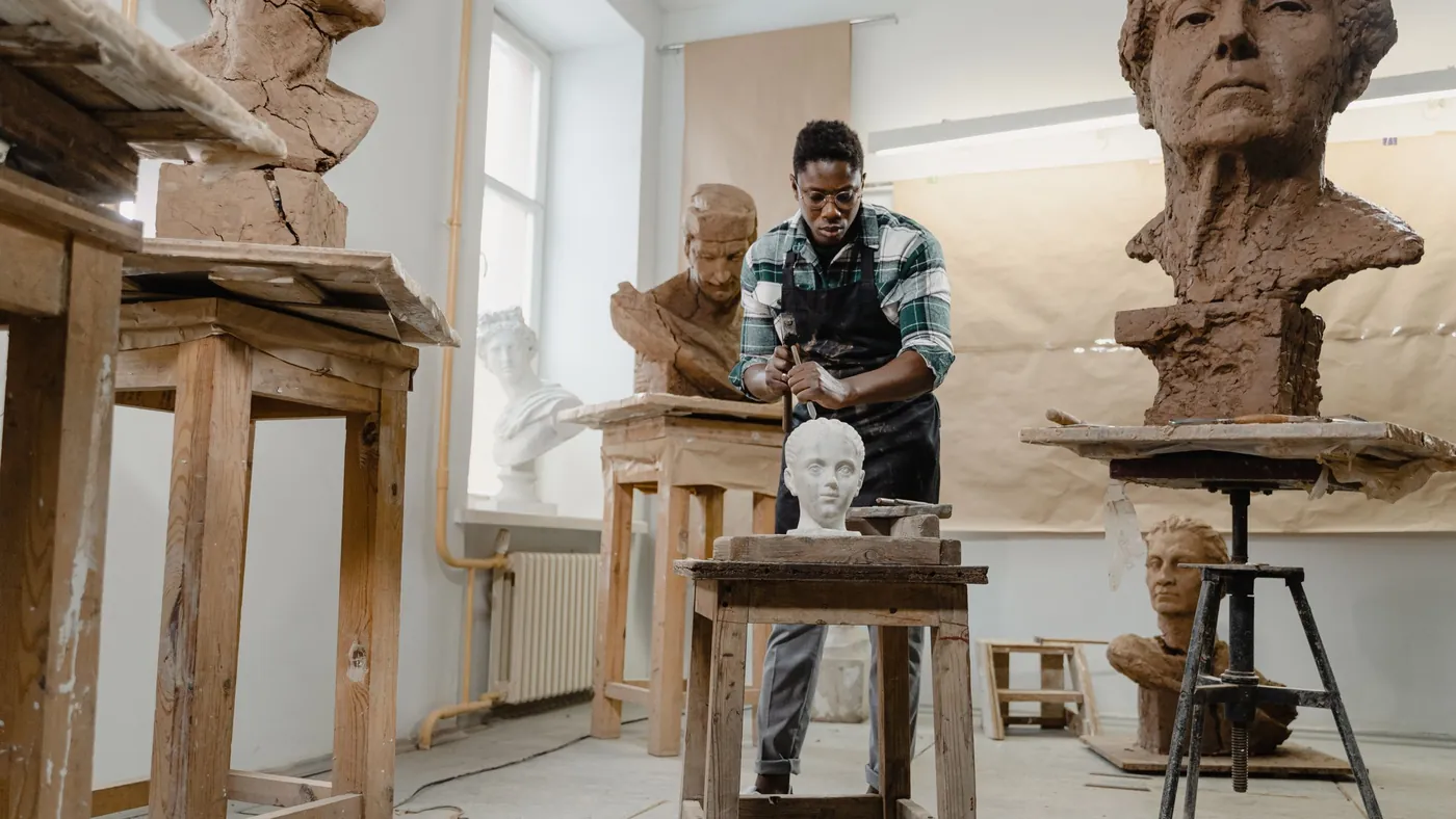 Un atelier de sculpture lumineux : un sculpteur travaille parmi des bustes en argile posés sur des sellettes en bois