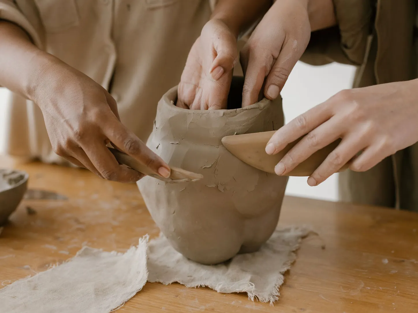 Plusieurs mains façonnent ensemble un pot en argile sur une table d'atelier
